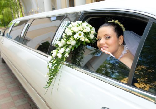 Image of beautiful bride showing her rose bouquet out of wedding limousine and looking at camera